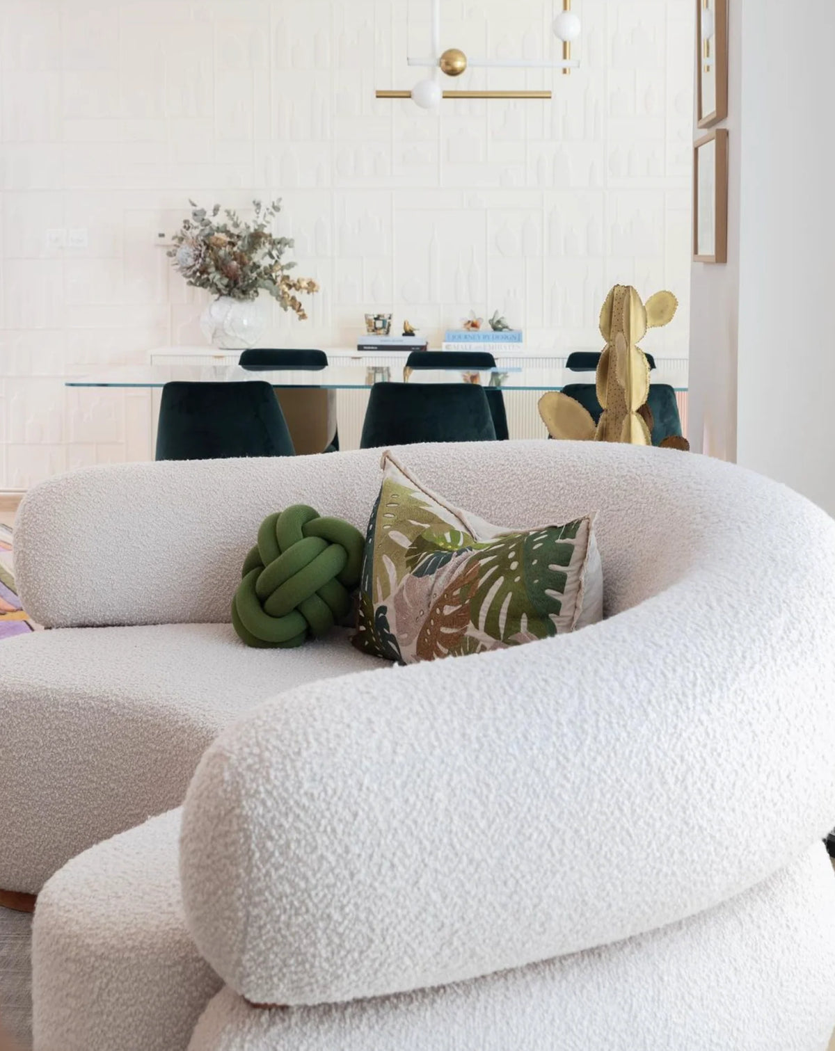 Curved white bouclé sofa with knot and leaf print cushions in a bright living room
