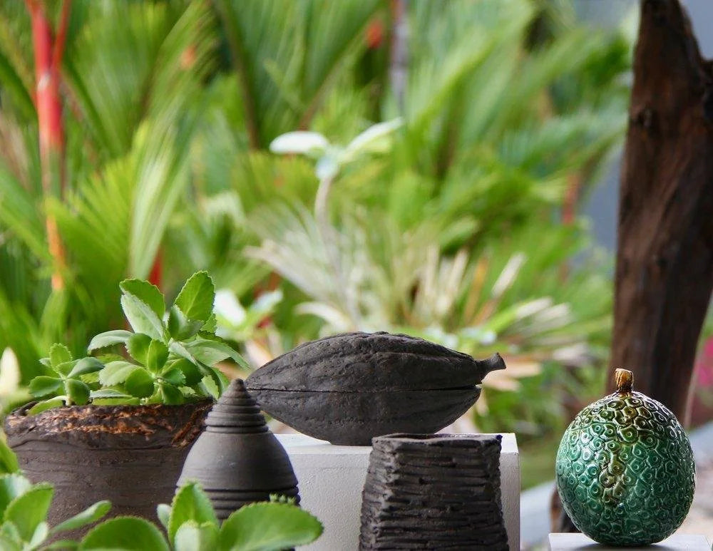 Dark ceramic sculptures and potted plants arranged in a tropical garden
