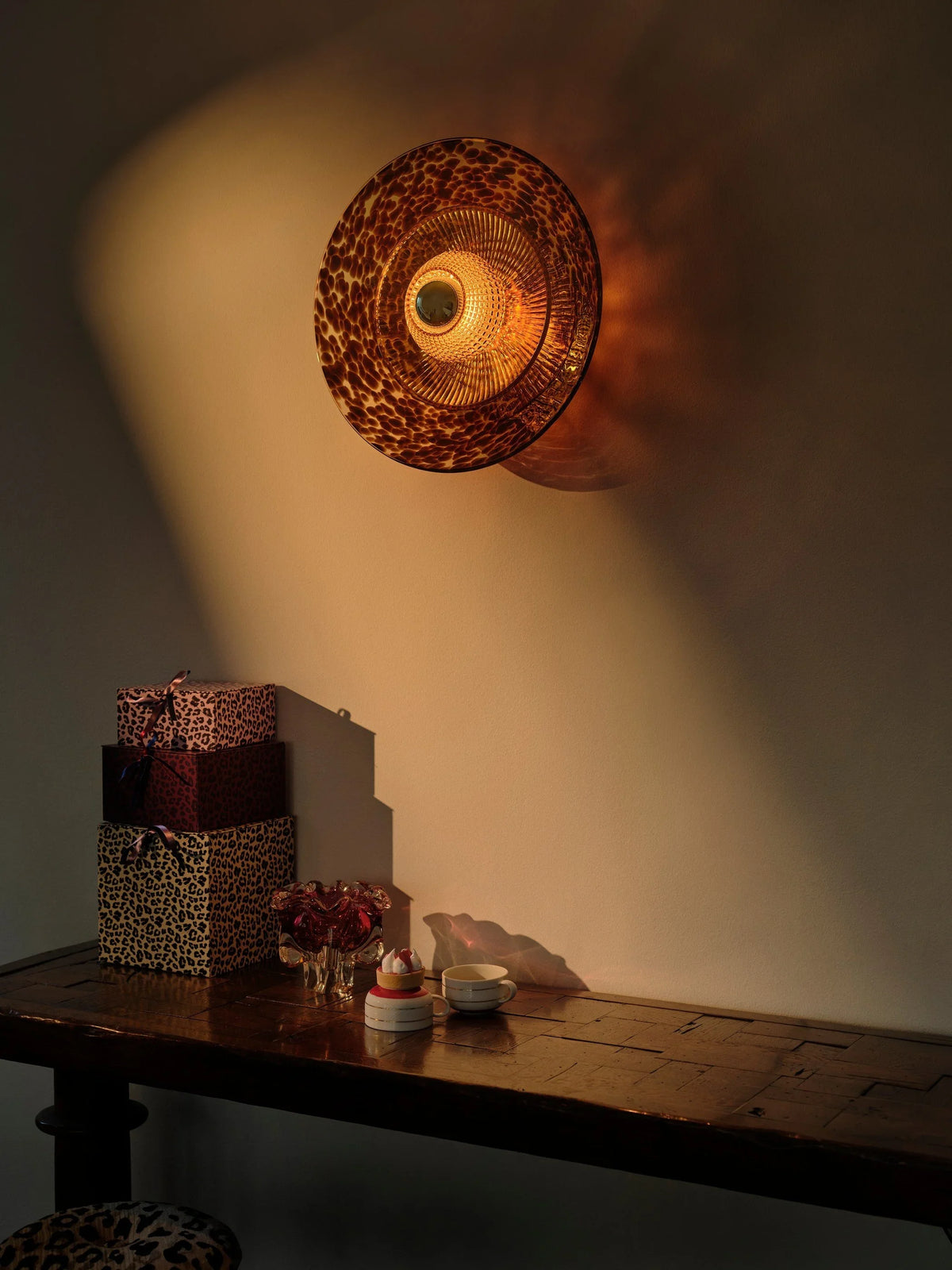 Glass wall sconce glowing above a walnut console table in a fall-styled entry by Maison Burgos