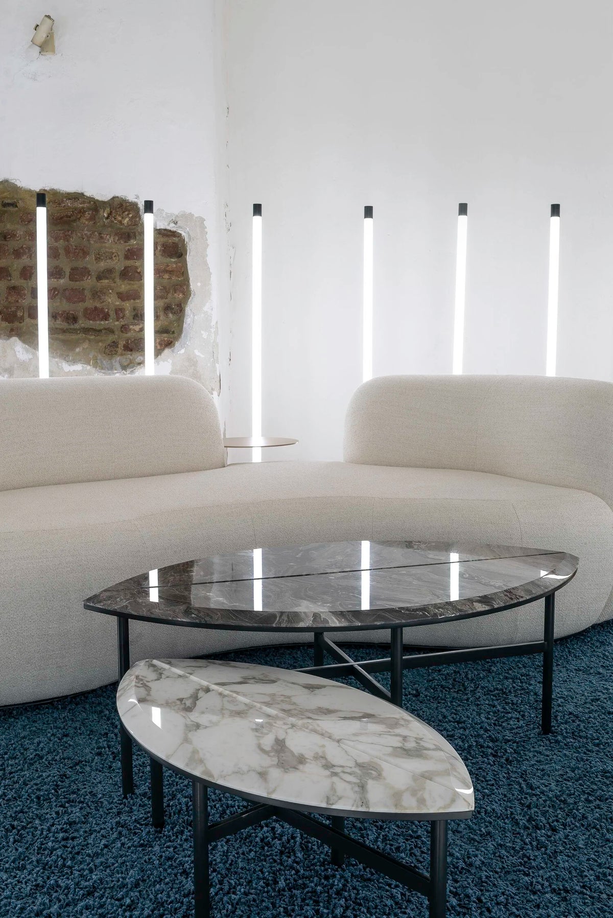 Oval black marble and white marble nesting coffee tables in front of a curved white sofa