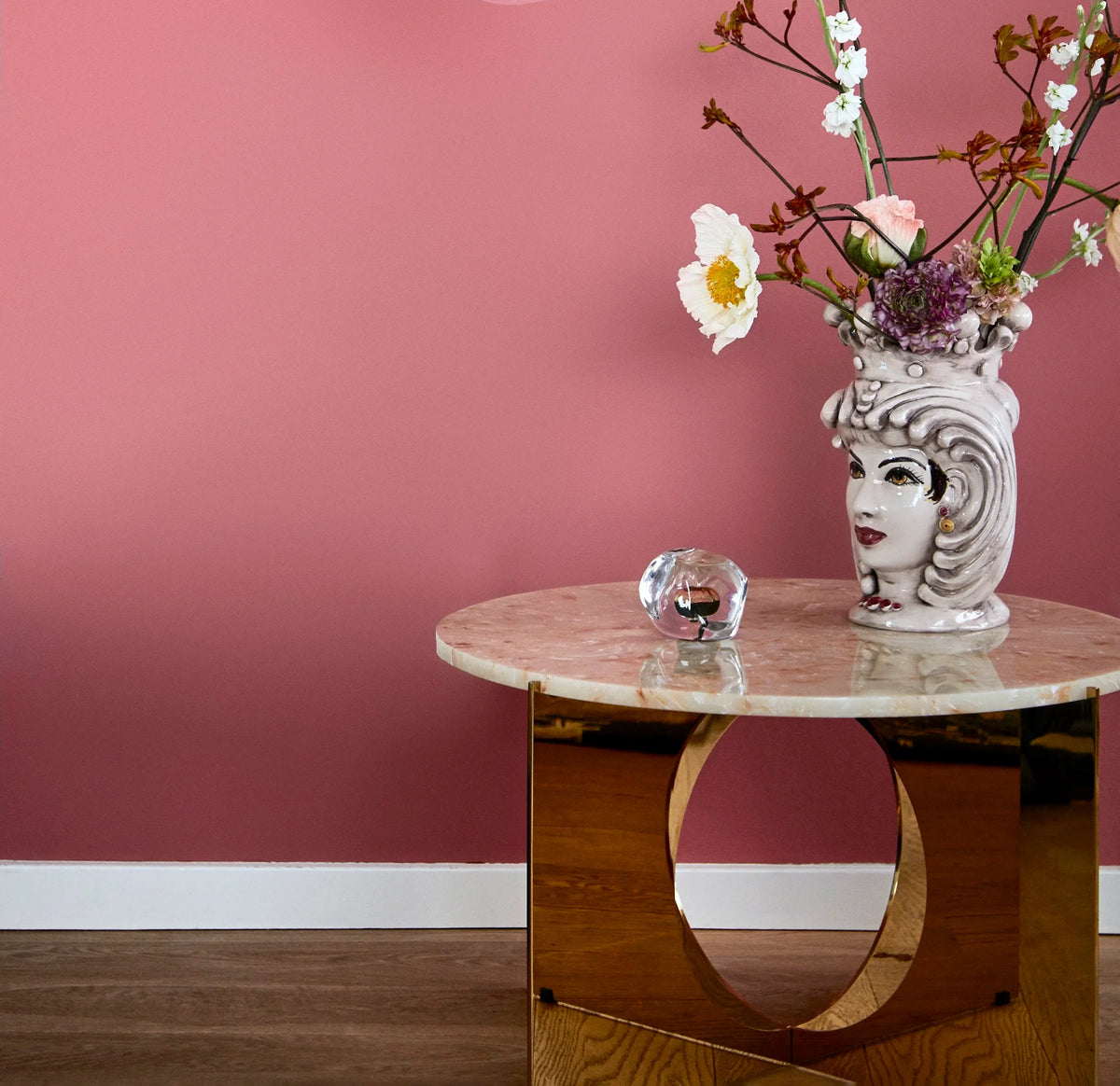 Pink marble side table on a brass ring base with a sculptural head vase and flowers