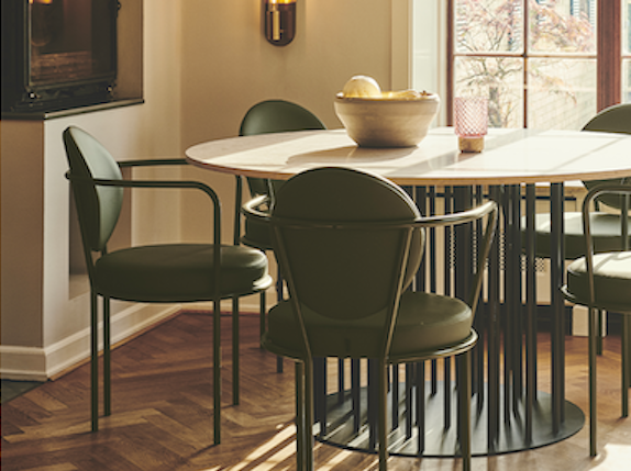 Round dining table with dark green upholstered armchairs in a sunny city apartment