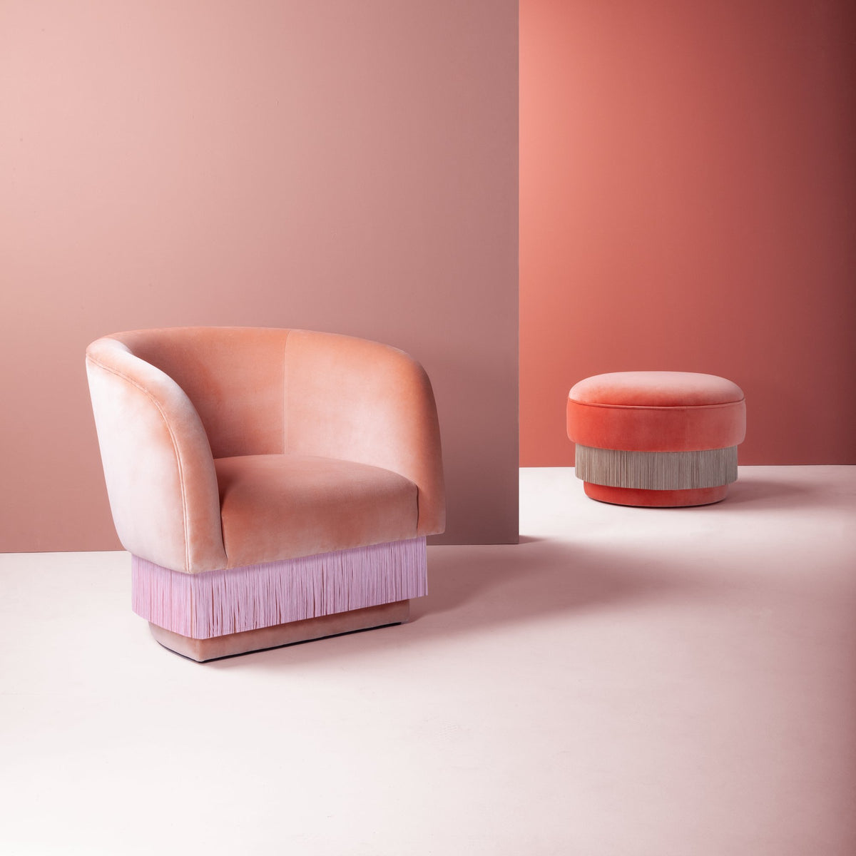 La Folie Armchair in pink velvet beside a matching fringed pouf in a pink room
