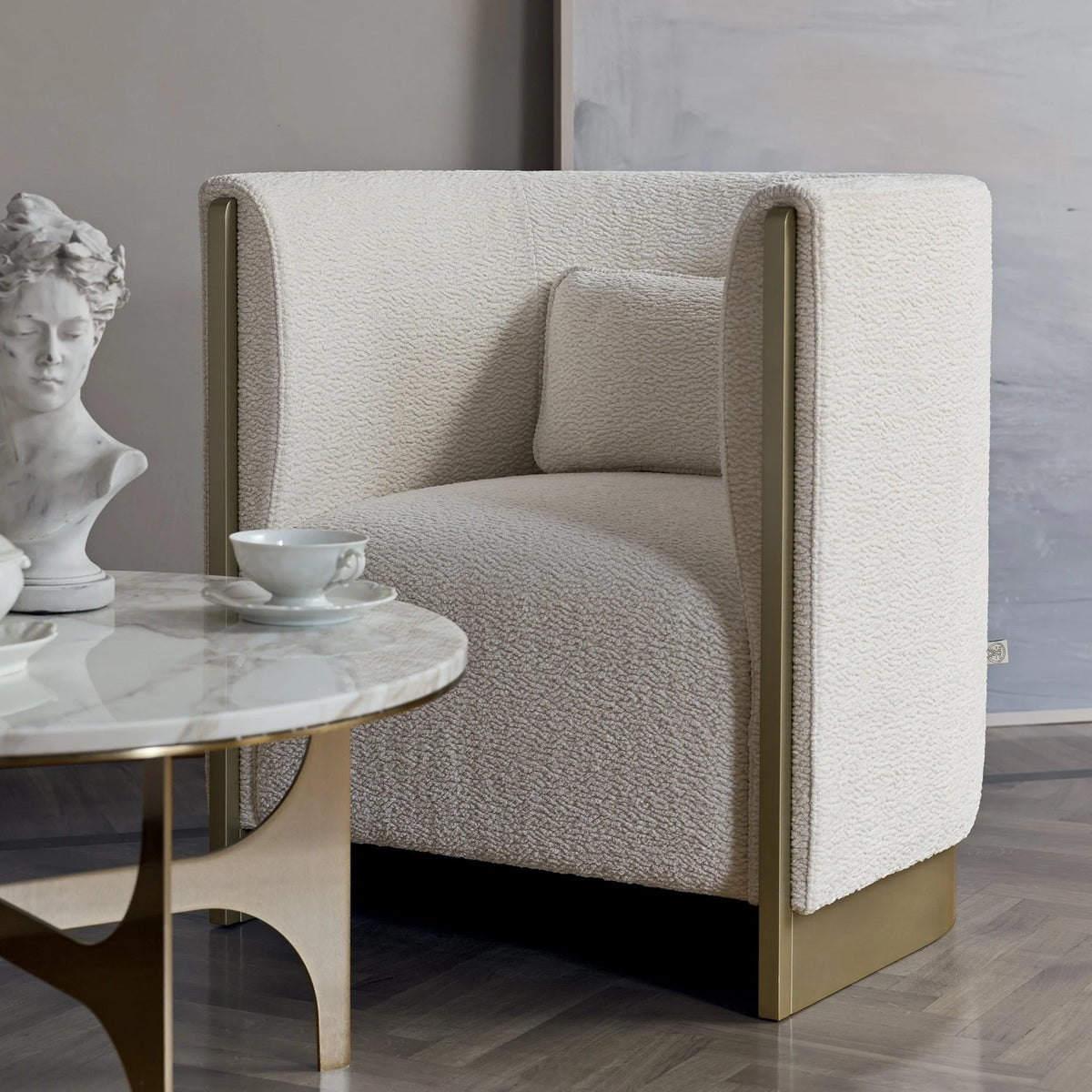 Adeline Armchair in ivory beside a marble side table and sculpture bust