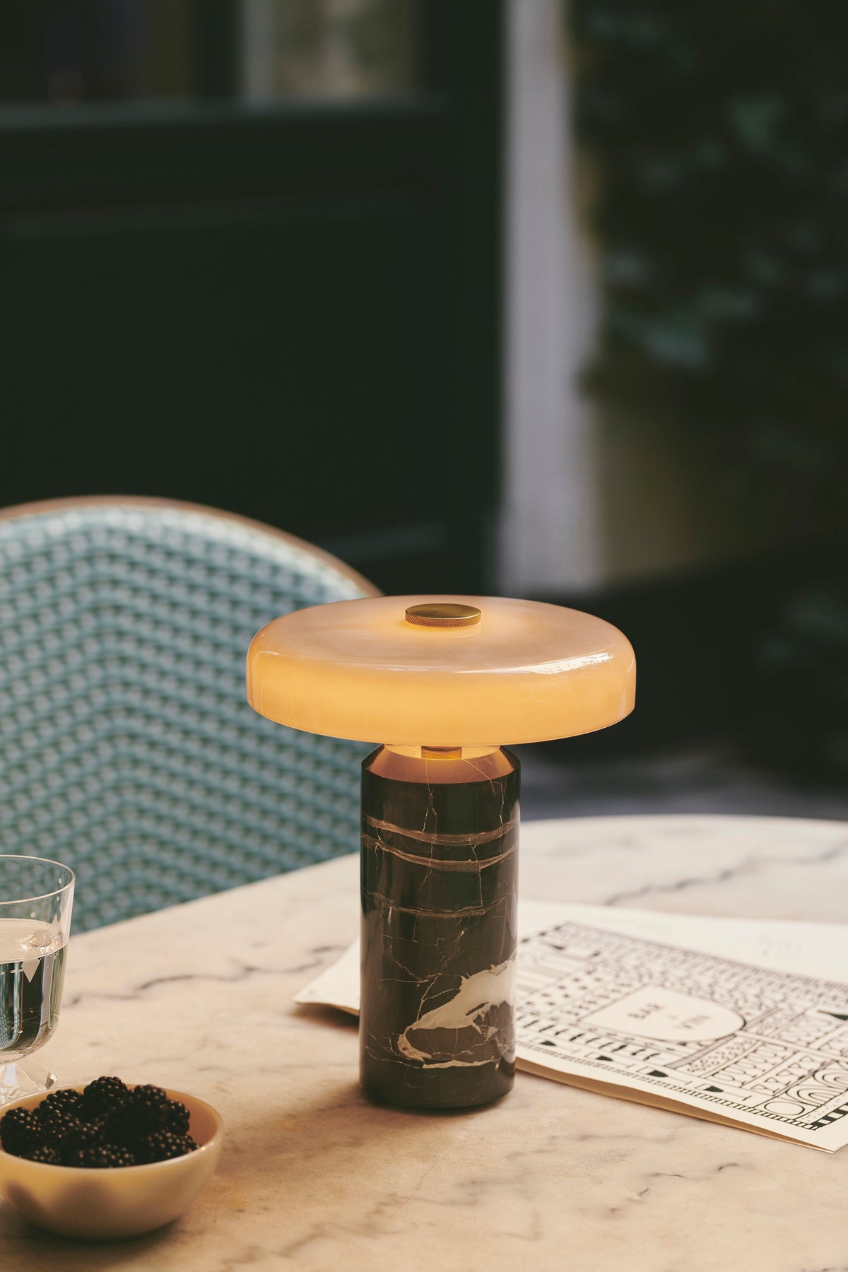 Trip Table Lamp lit with amber glow on a marble table outdoors, close view