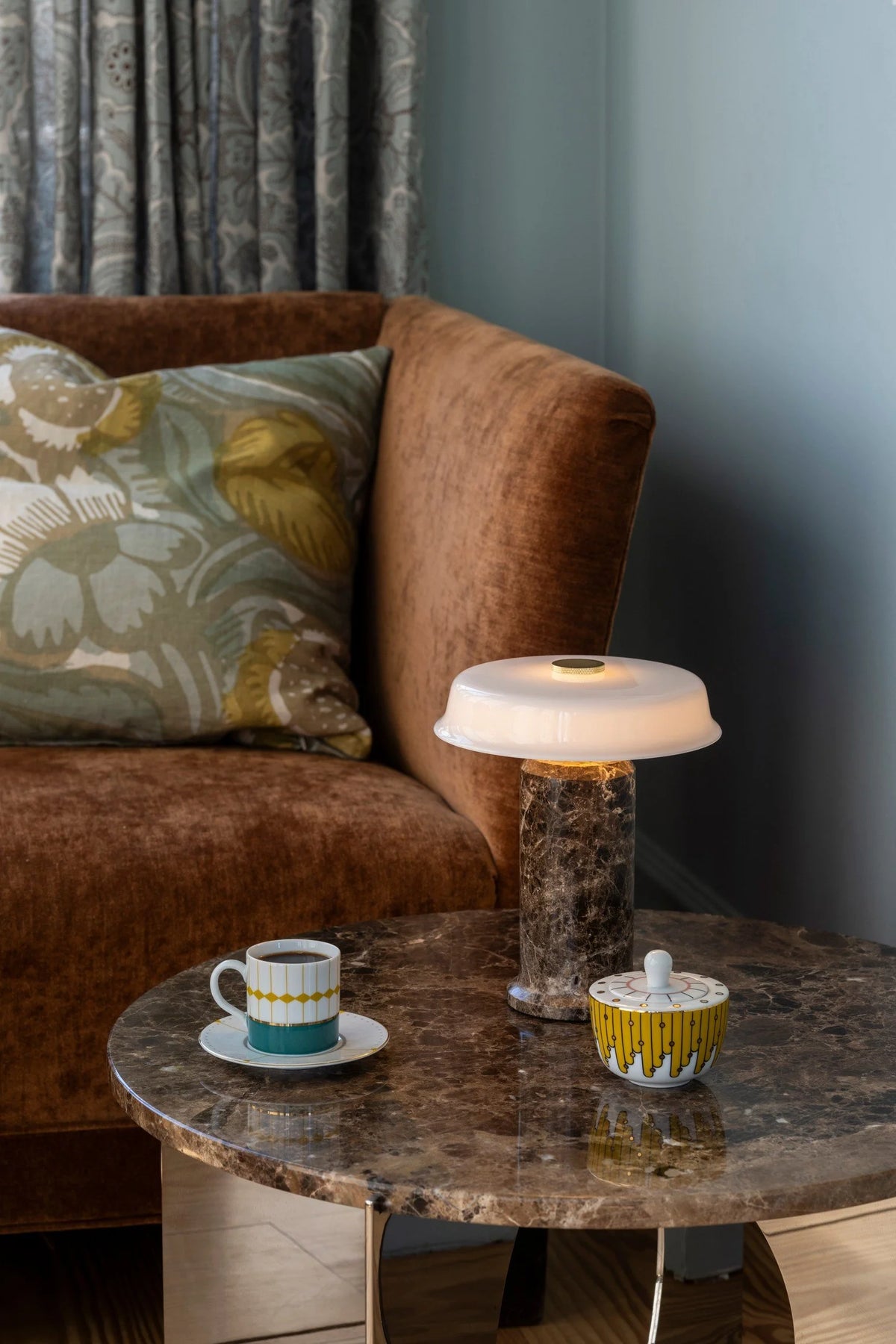 Trip 2 Table Lamp in Dark Emperador / Opal lit on a marble side table beside a rust velvet sofa