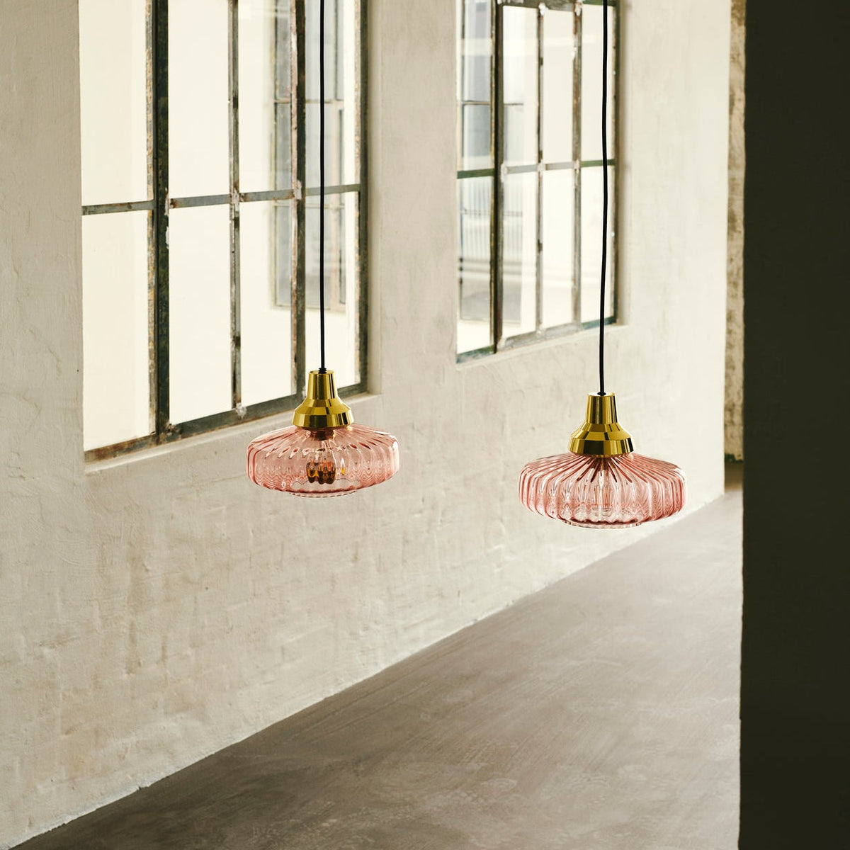 New Wave Optic Pendant Light Pink pair in pink glass with gold canopies by loft windows