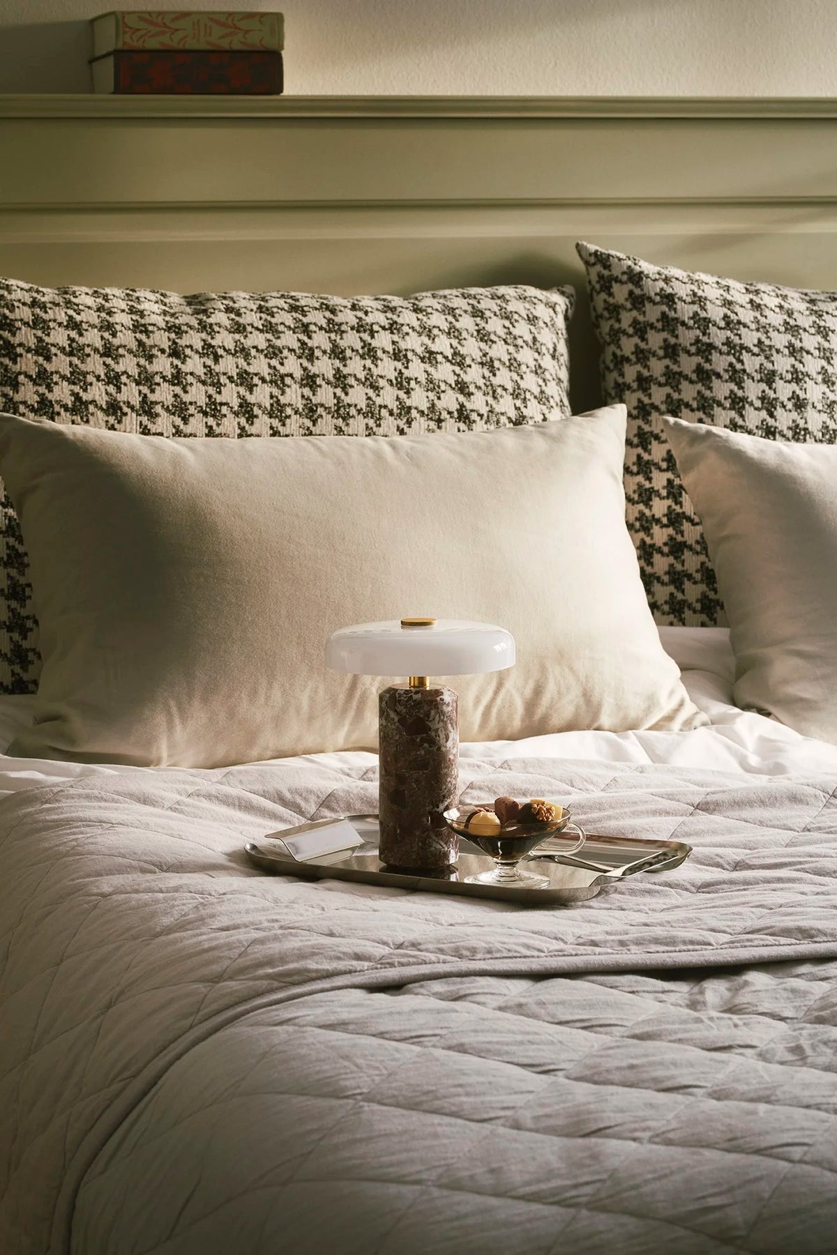 Trip Table Lamp in Burgundy / Opal switched off on a tray on a made bed