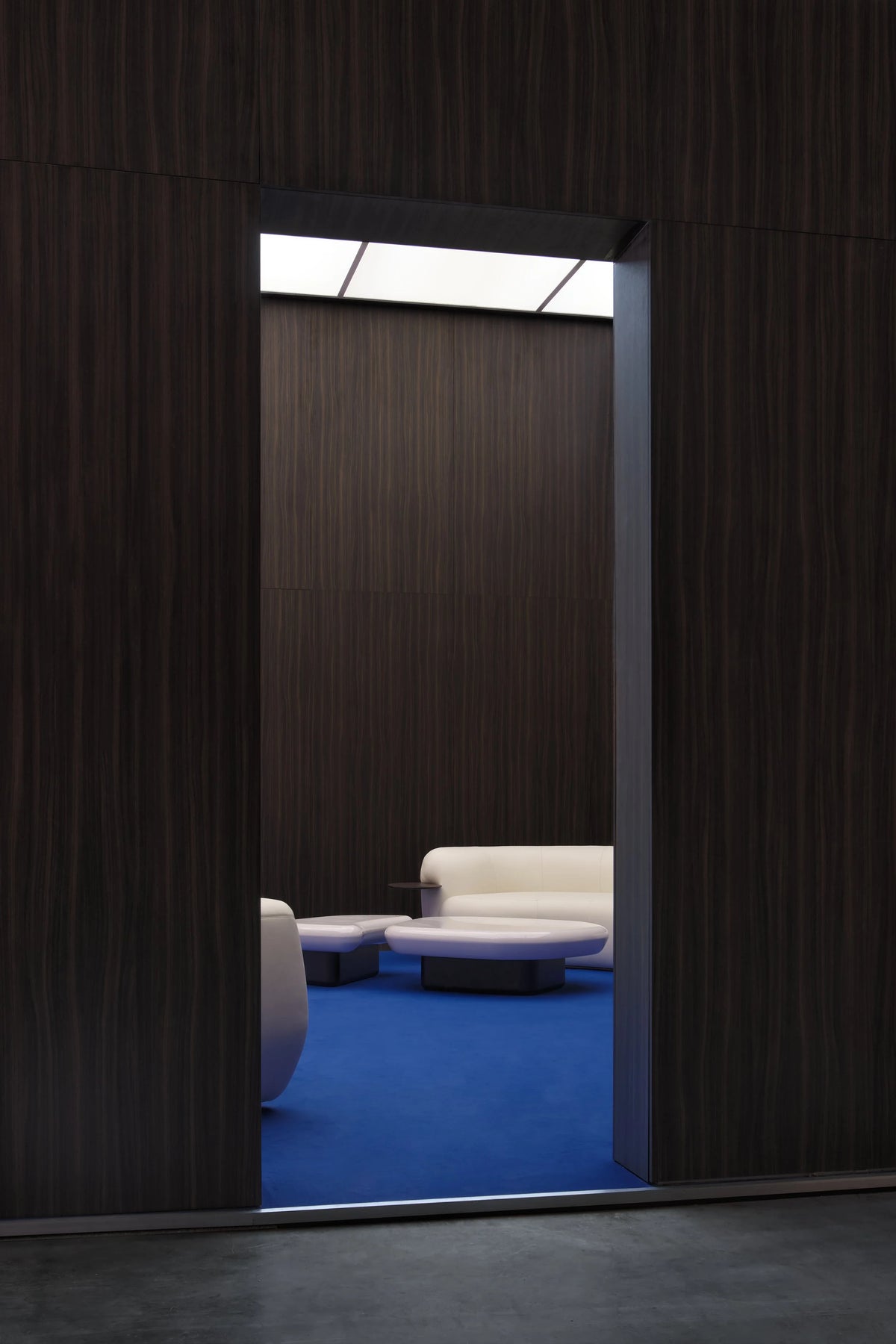 Kawa Coffee Tables seen through a dark wood doorway in a blue-carpeted lounge