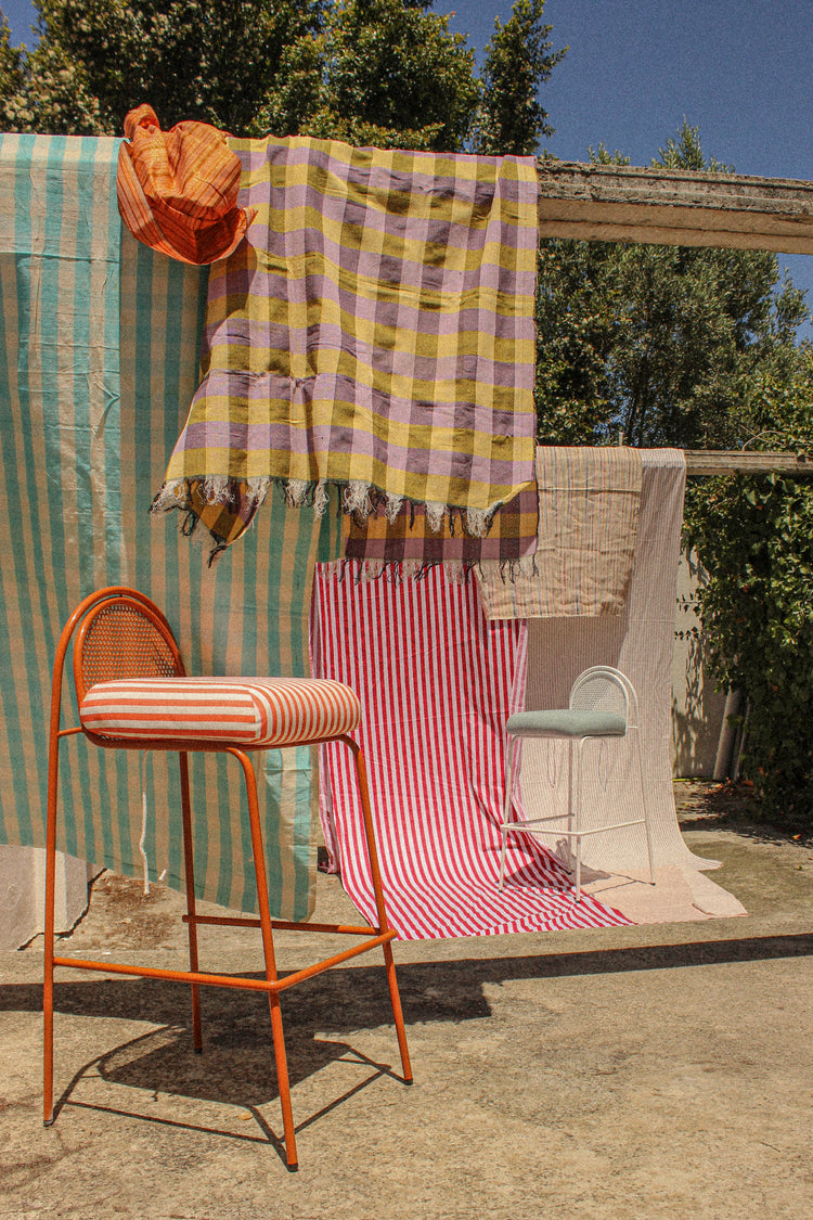 Riviera Bar Chair in copper with striped seat among draped outdoor textiles