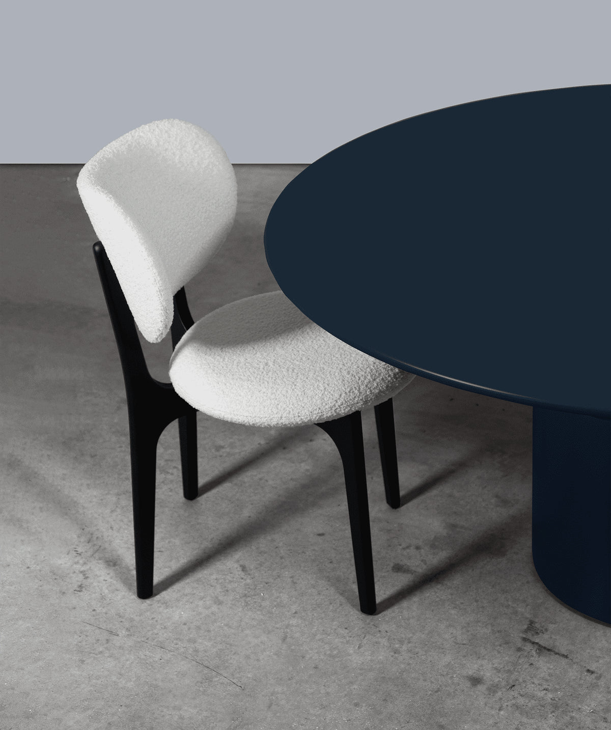 Silo Dining Table in navy lacquer, close view of the edge beside a white boucle chair