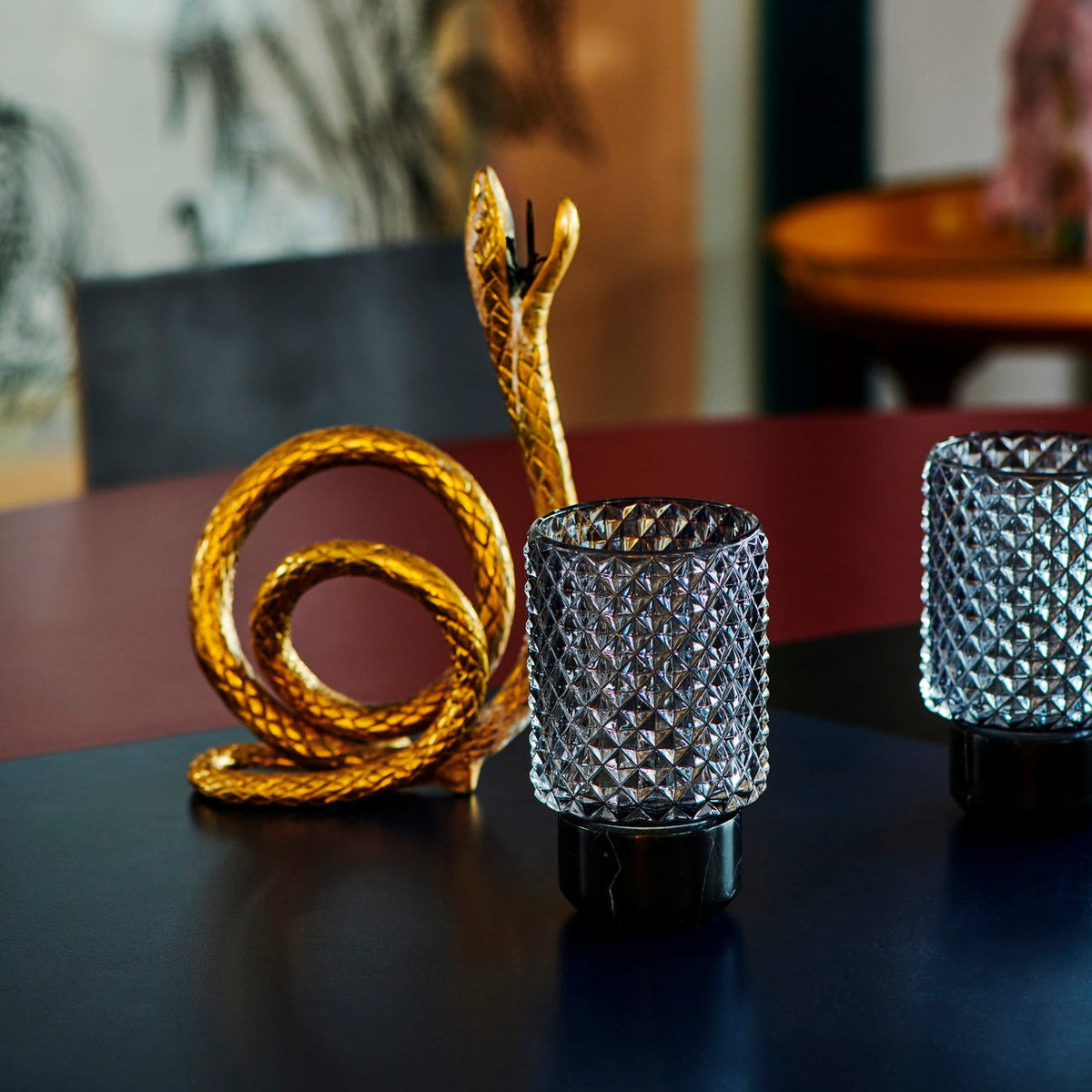 Sons of Marble Candle holder hurricane in Smoke beside a gold snake sculpture on a dark table