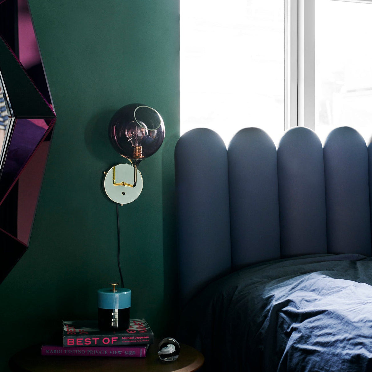 Ballroom Wall Sconce in purple glass on a green wall beside a channel-tufted headboard
