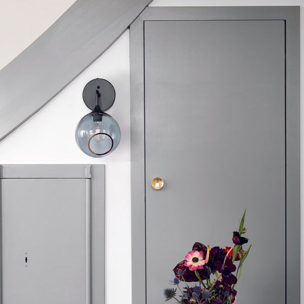 Ballroom Wall Sconce in Smoke glass on a grey wall beside a door with flowers