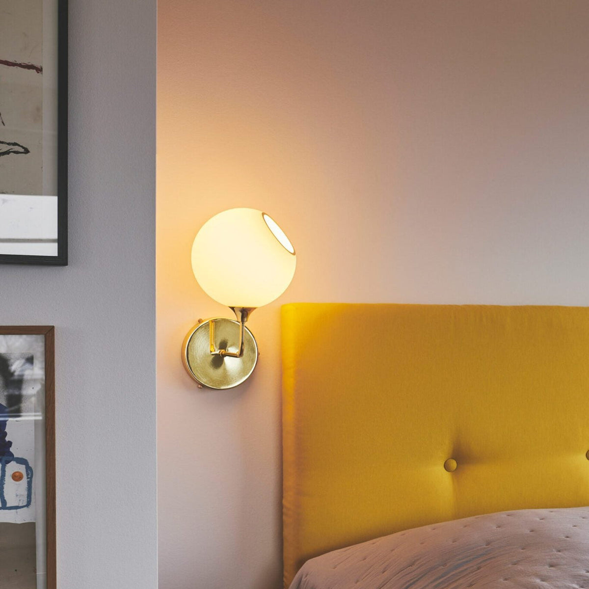 Ballroom Wall Sconce lit with opal globe and brass arm beside a yellow headboard