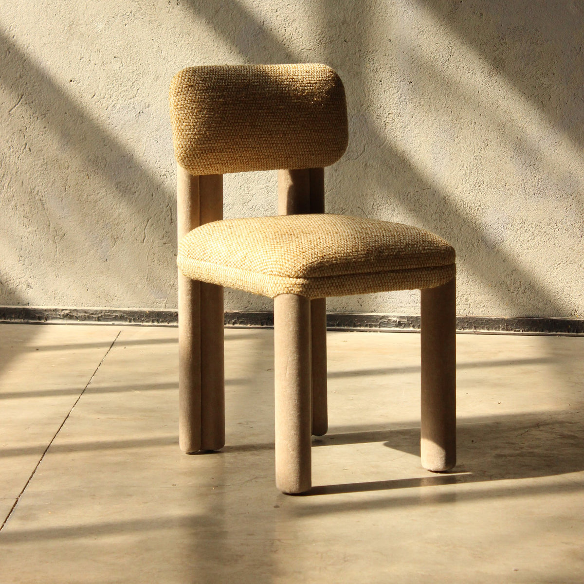 Camelia Dining Chair in mustard bouclé with sunlit shadows on a concrete wall