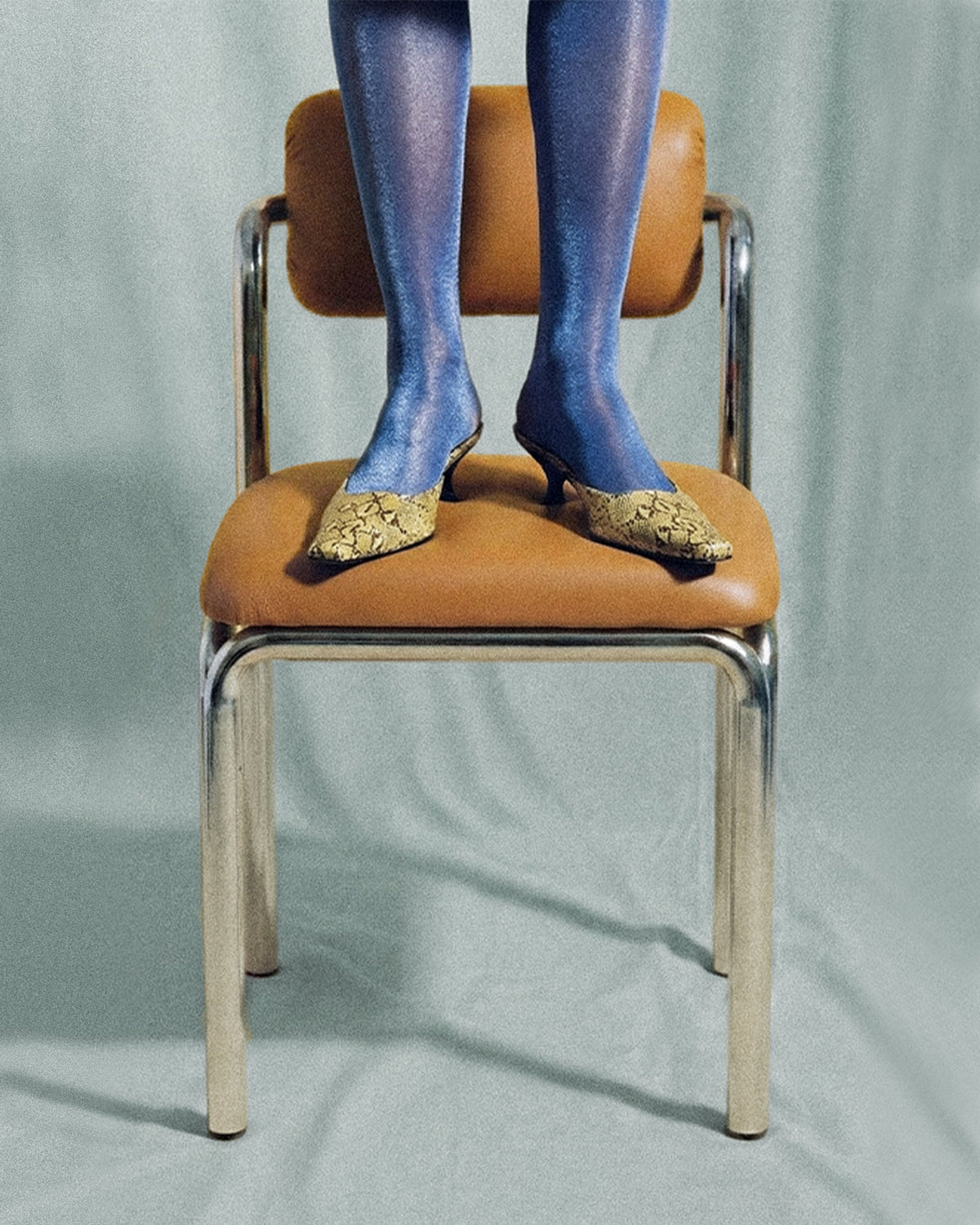 Cubu Chair with tan leather seat and polished nickel frame, styled with a model's feet