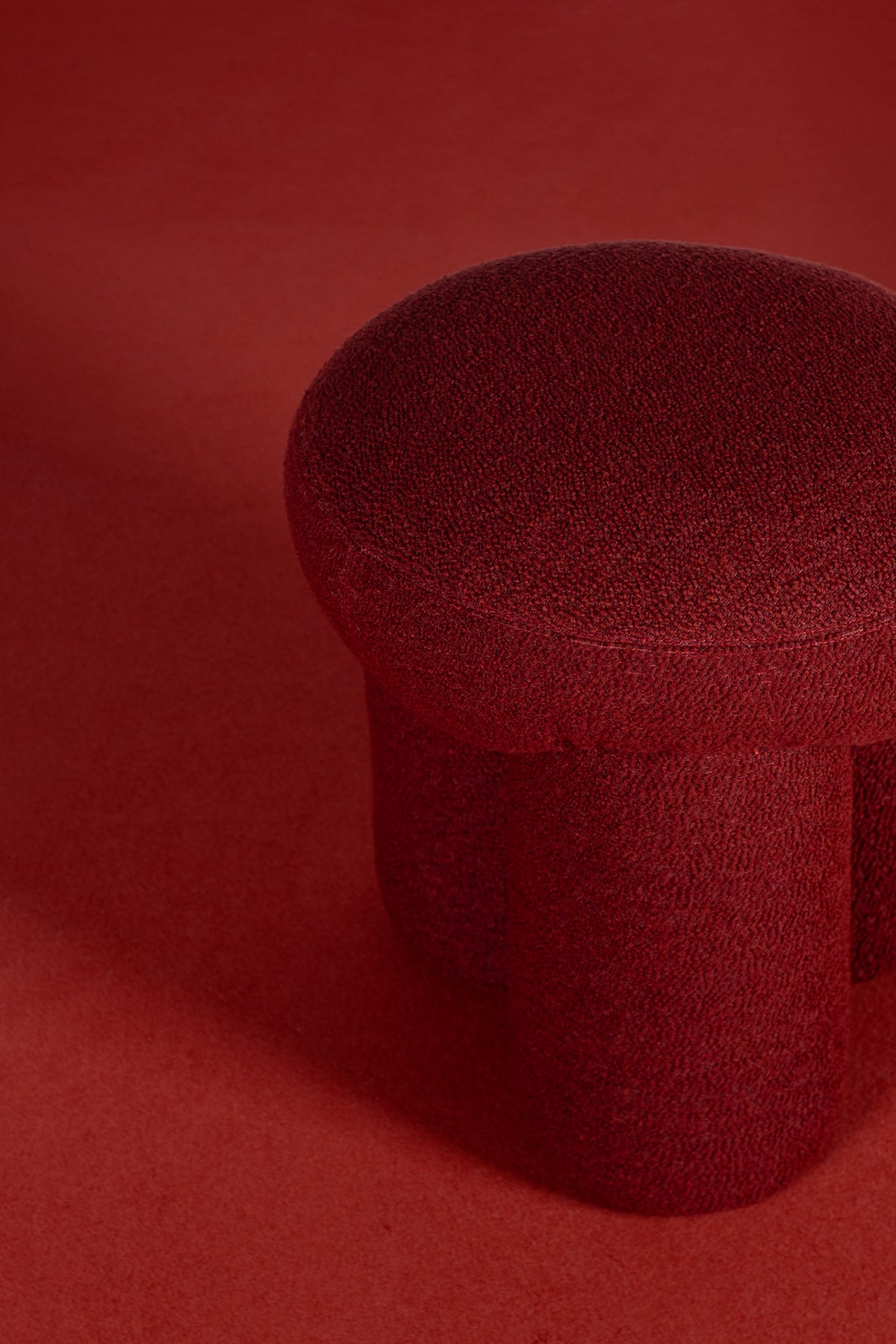 Douglas Ottoman close-up in red bouclé against a red backdrop