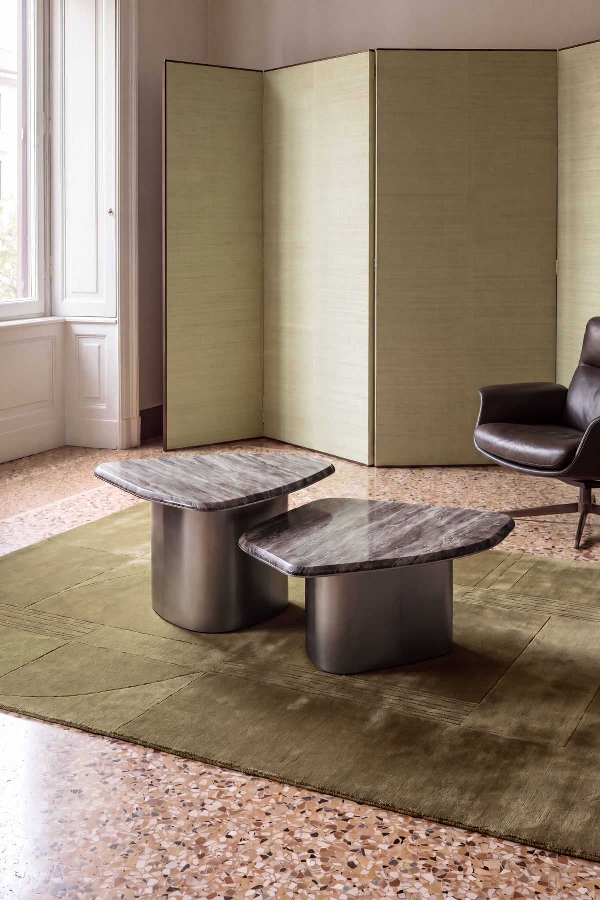 Fragment Coffee Tables in grey marble on a green rug in a terrazzo-floored room