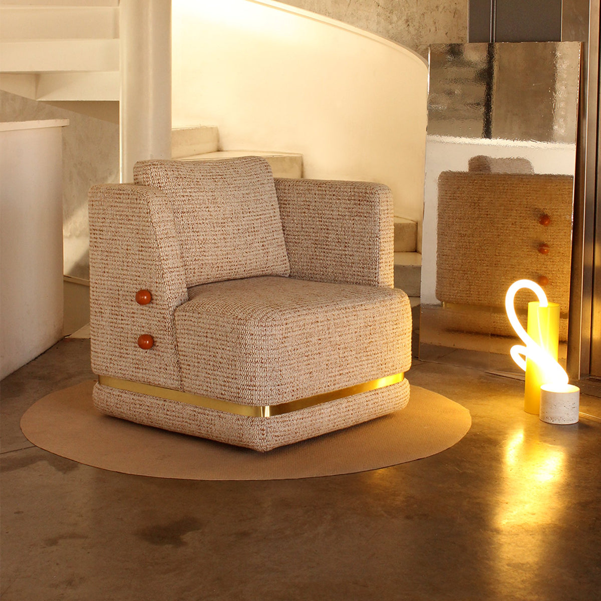 Panorama Armchair in speckled bouclé on a round rug beside a glowing lamp