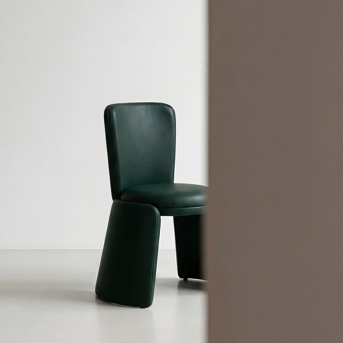Inge Chair in dark green leather beside a brown wall panel