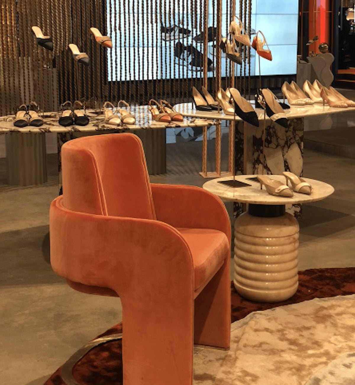 Jean Side Table with white marble top beside an orange velvet chair in a shoe boutique