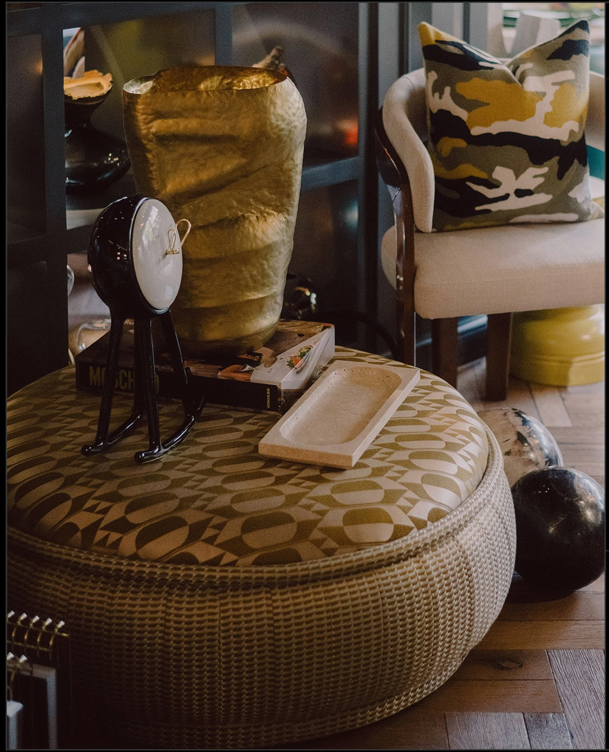 Malibu Ottoman in gold patterned upholstery styled with sculptures and books