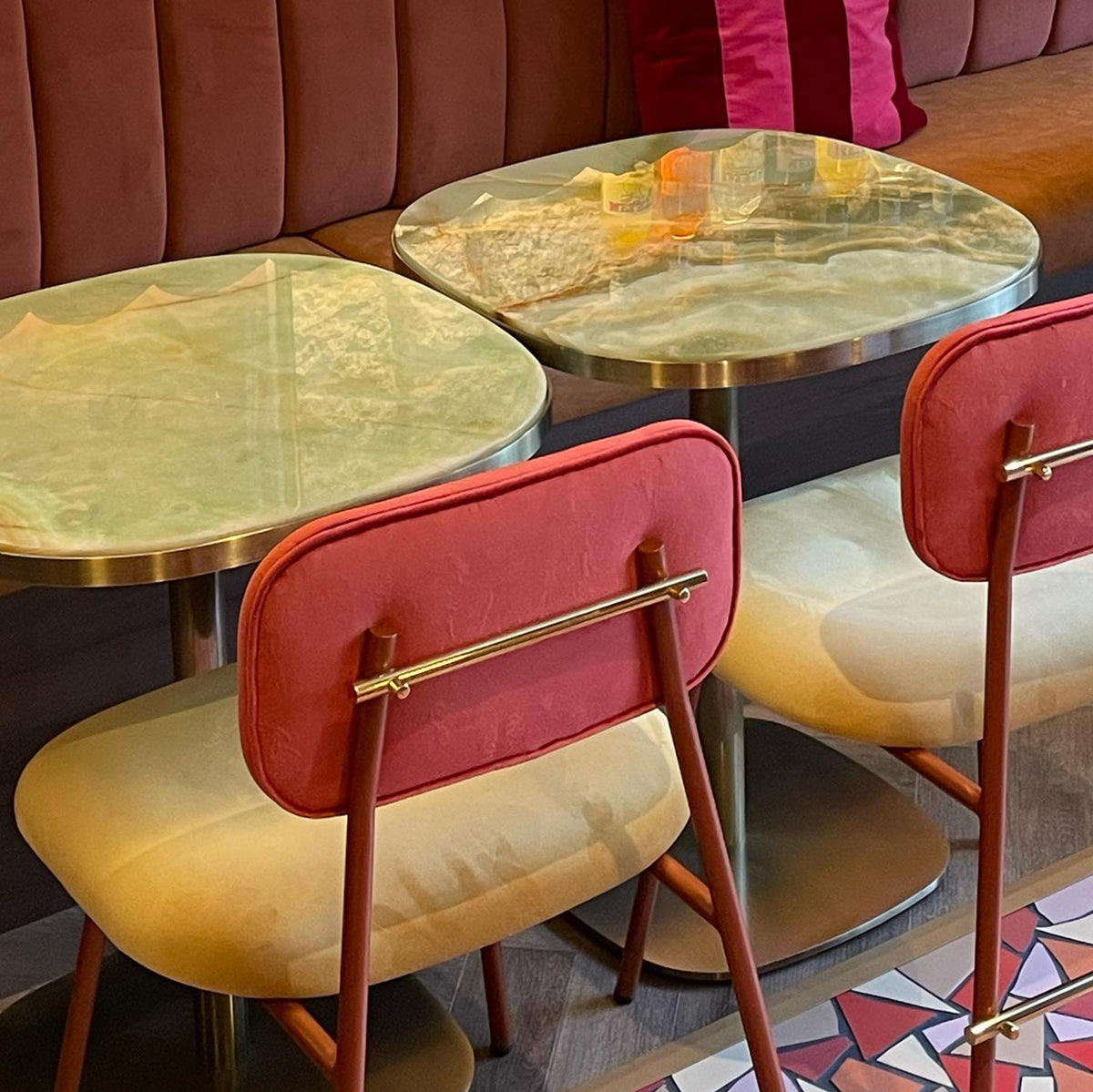 Miami Dining Chairs in coral velvet with brass back rails at onyx-topped tables