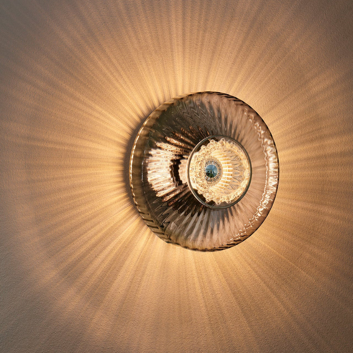 New Wave Optic Wall Sconce XL in Smoke glass lit on a wall, front view