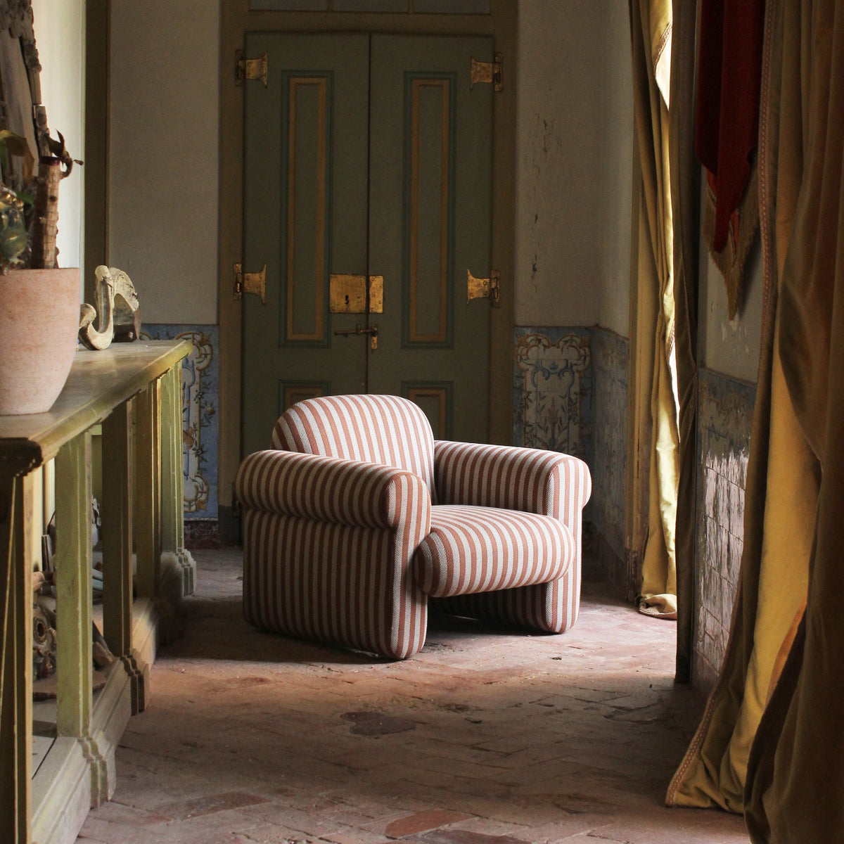 Oscar Armchair in rose stripes in a historic room with green doors and tiled walls