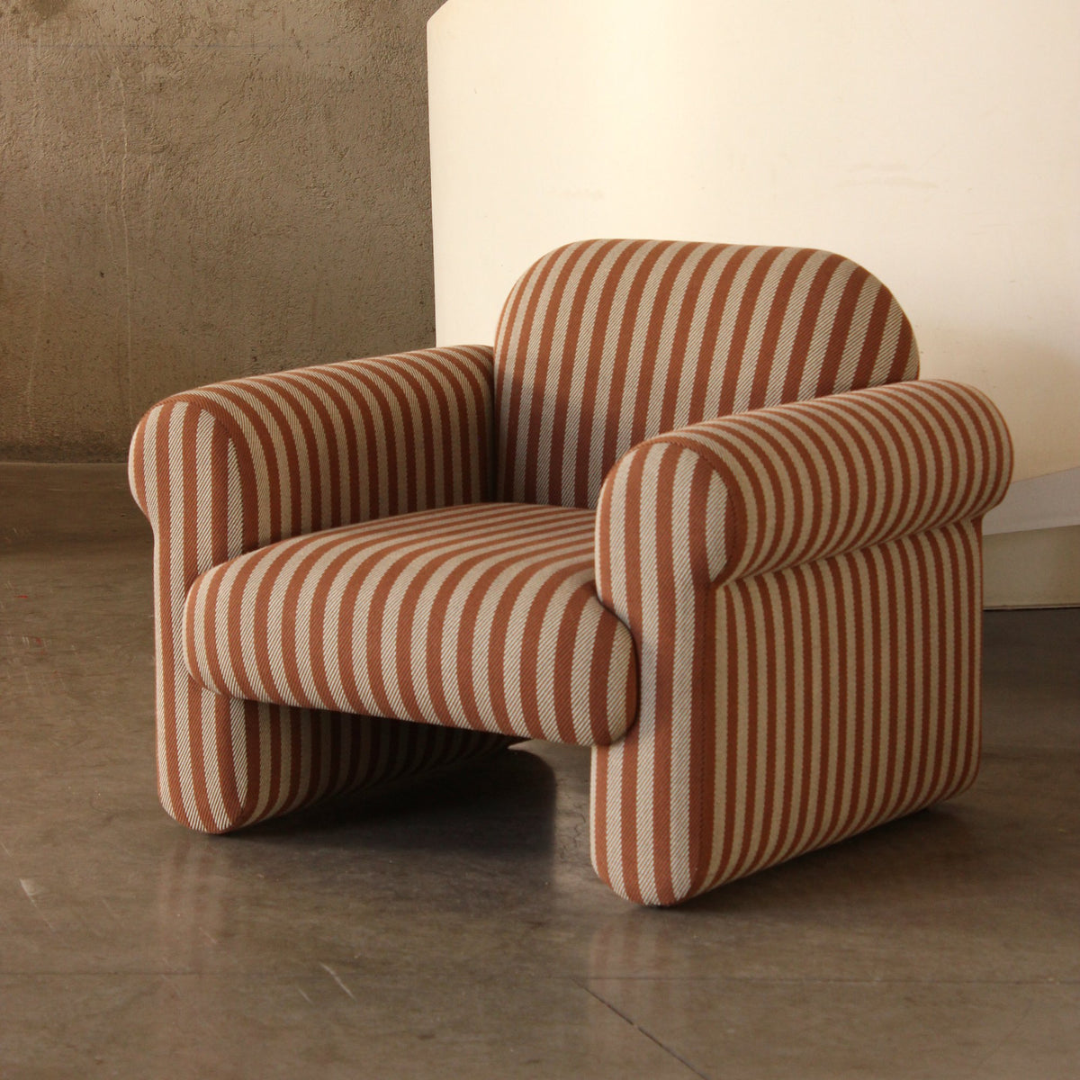 Oscar Armchair in rust and cream stripes in a concrete-walled room