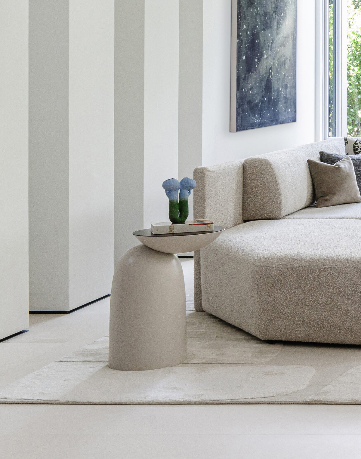 Pingu Side Table in taupe lacquer beside a beige sofa with a vase of blue flowers