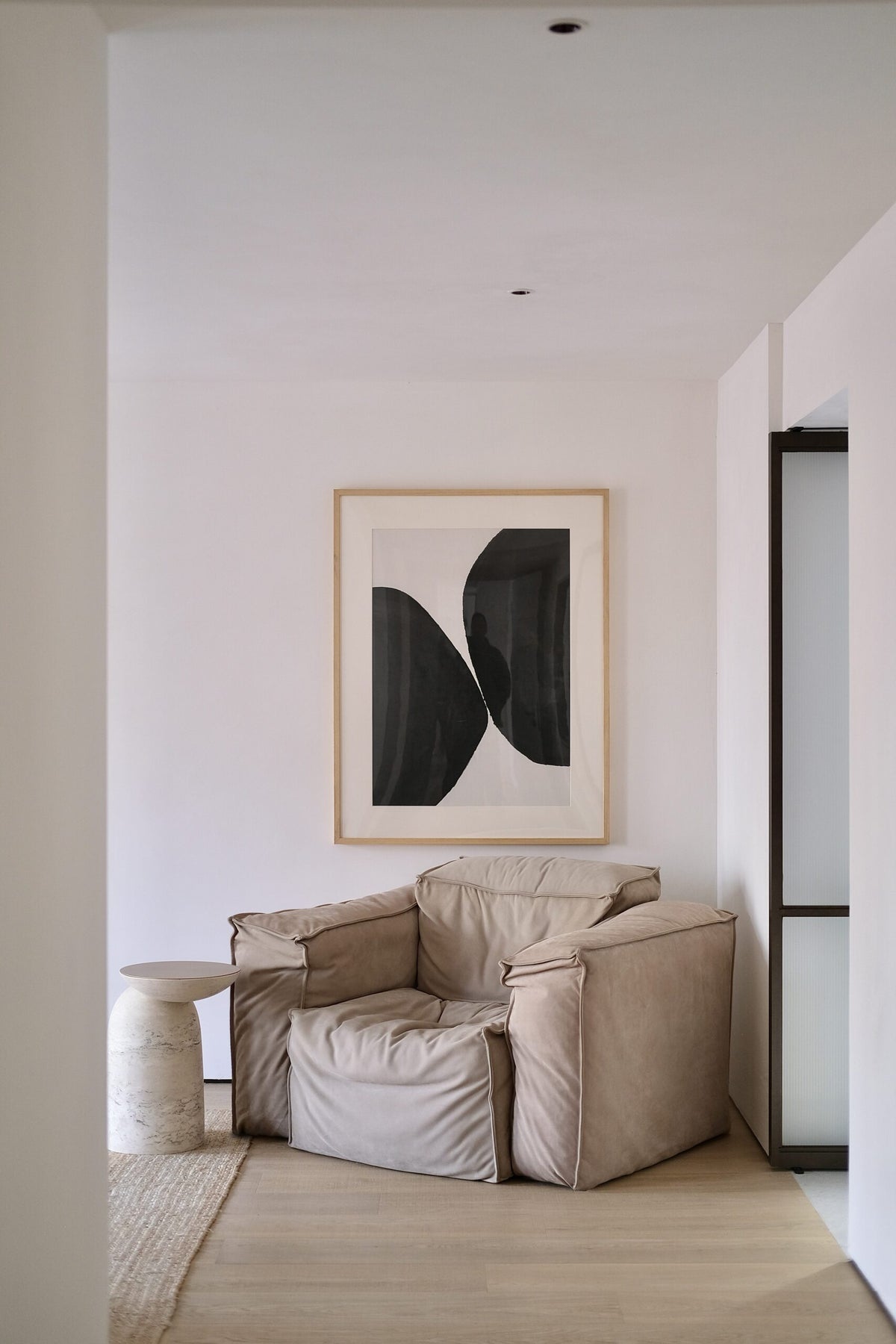 Pingu X Side Table in Travertino beside a slouchy leather armchair in a white room