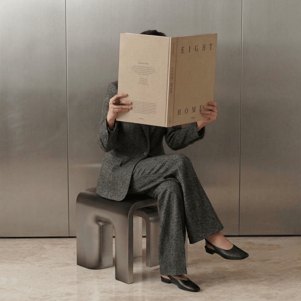 Plié Side Table in Polished Inox used as a seat by a person reading a magazine