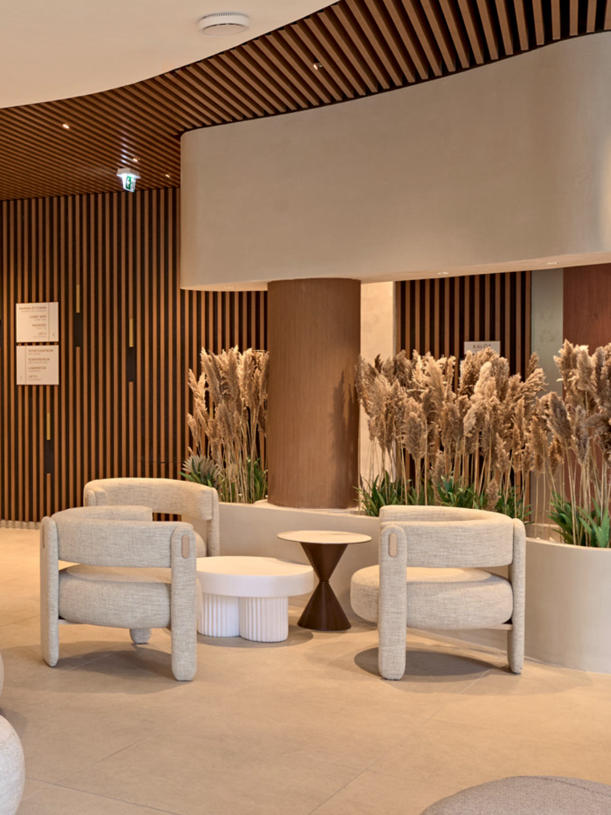 Choux Armchair pair with a white side table in a lobby with wood slat walls and pampas grass
