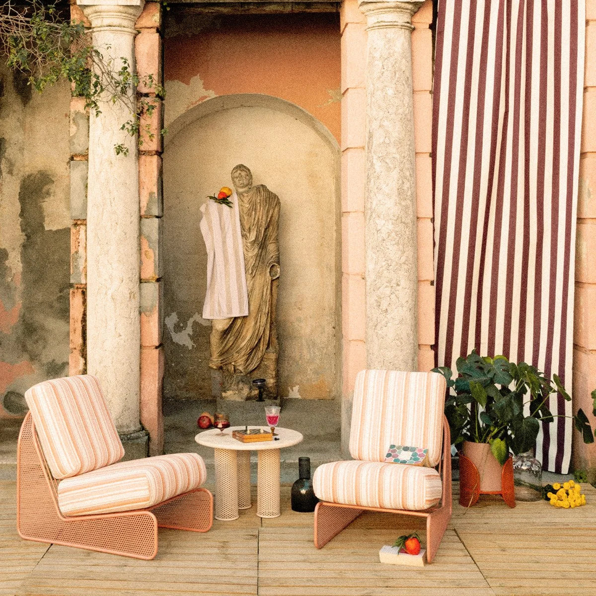 Riviera Armchair pair in pink stripe in a courtyard with a statue and striped curtain