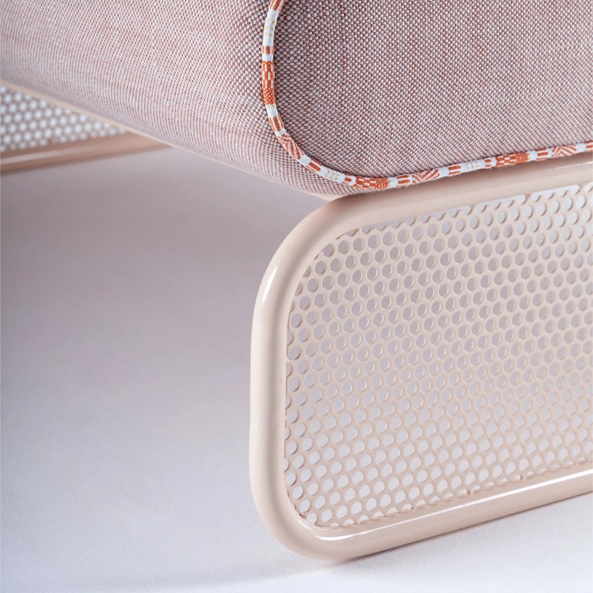 Riviera Modular Sofa - 1 Seat close-up of the perforated metal base under a blush cushion with piping