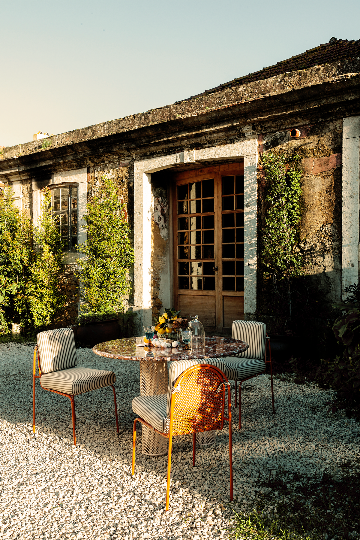 Riviera Dining Table outdoors by a stone cottage at golden hour