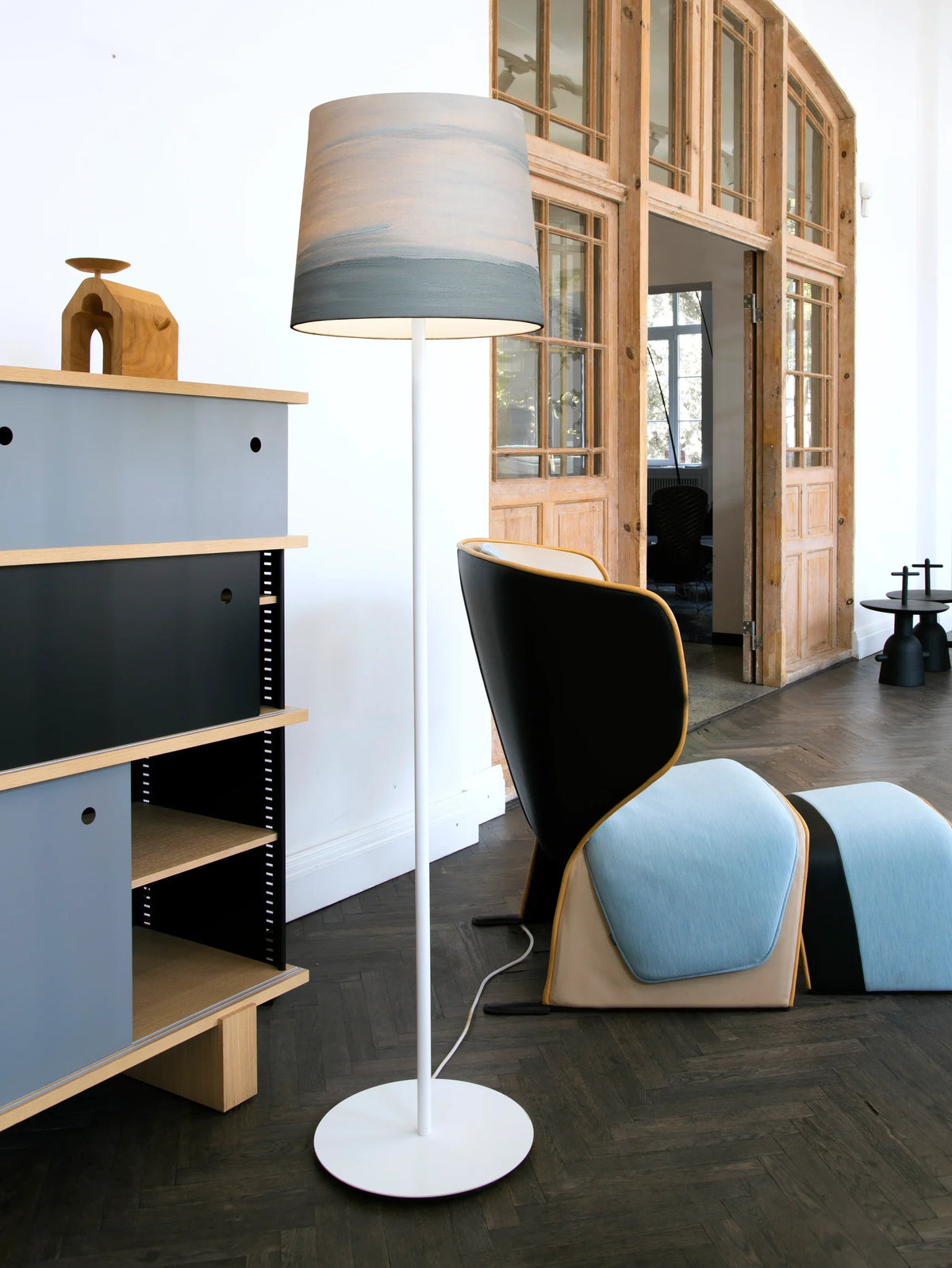 Mammalampa Sisters Floor Lamp in Fog beside a wing chair and blue shelving in a loft