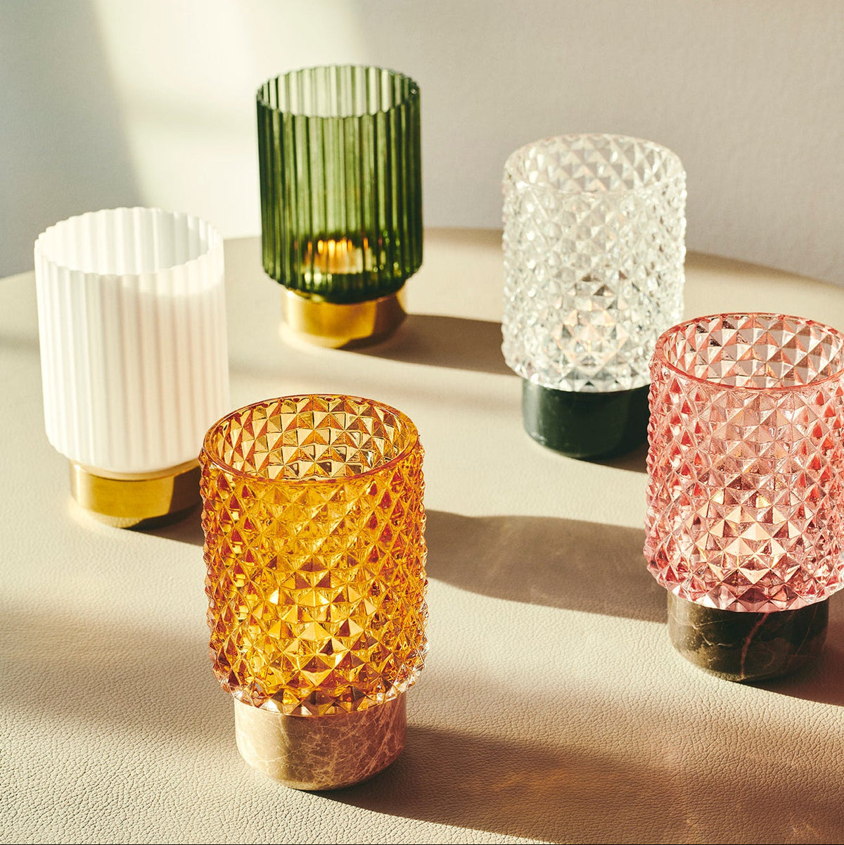 Sons of Marble Candle holder hurricane in Amber with Rose, Clear and green glass on a sunlit table