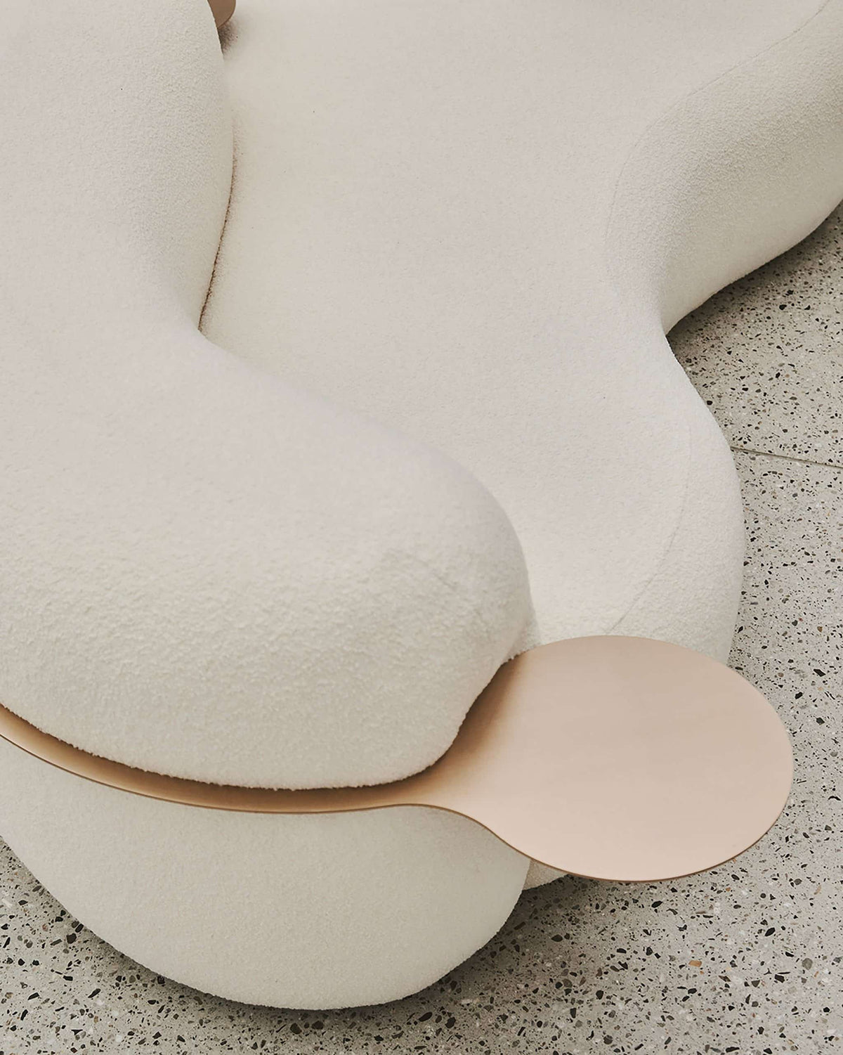 Tateyama Curved Sofa, close-up of the boucle arm and copper-tone tray on terrazzo