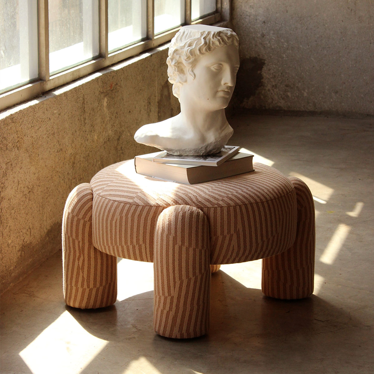 Marlon Pouf in striped weave with a sculpted bust in a sunlit room