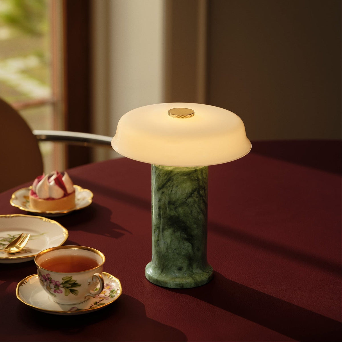 Trip 2 Table Lamp with green marble base and opal shade, lit on a dining table set for tea