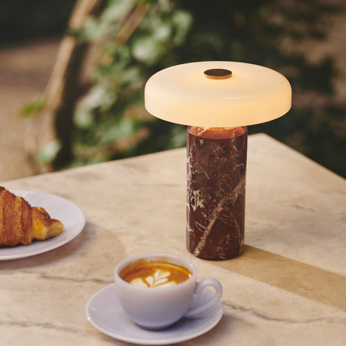 Trip Table Lamp – Burgundy | Opal lit on a café table with coffee and a croissant