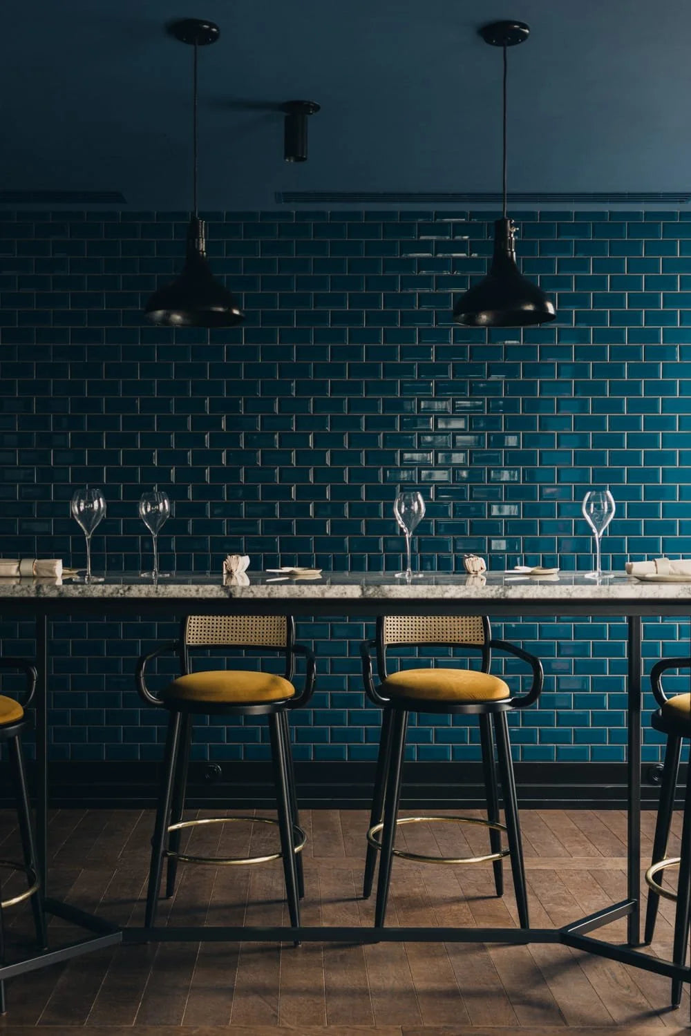 Luc bar chairs at a counter against teal subway tile